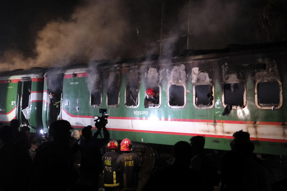 People stand near a burning passenger train at Gopibagh in Dhaka, Bangladesh, Friday, Jan. 5, 2024. A fire on a moving passenger train in Bangladesh's capital on Friday night left at least four people dead and several others injured, ahead of Sunday's parliamentary election. (AP Photo/Mahmud Hossain Opu)