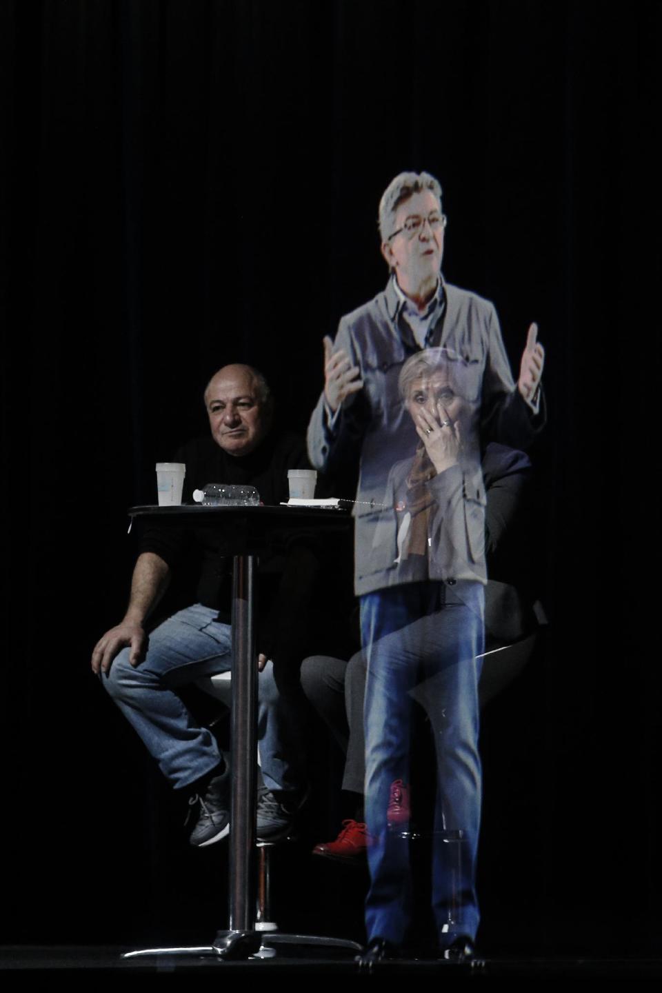 People sit at a table on stage and look towards the hologram of hard-left French presidential candidate Jean-Luc Melenchon, as he speaks to supporters who are gathered in Saint-Denis, near Paris, Sunday, Feb. 5, 2017. As Melenchon holds a rally in Lyon Sunday, a hologram of him is being projected by satellite to crowds in Paris. (AP Photo/Kamil Zihnioglu)