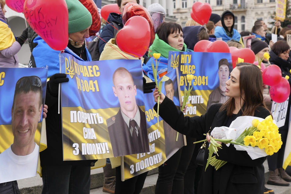 A woman gives out flowers at a gathering of family members of Ukrainian prisoners of war in Maidan Square in central Kyiv, Ukraine, Saturday March 16, 2024. (AP Photo/Tony Hicks)