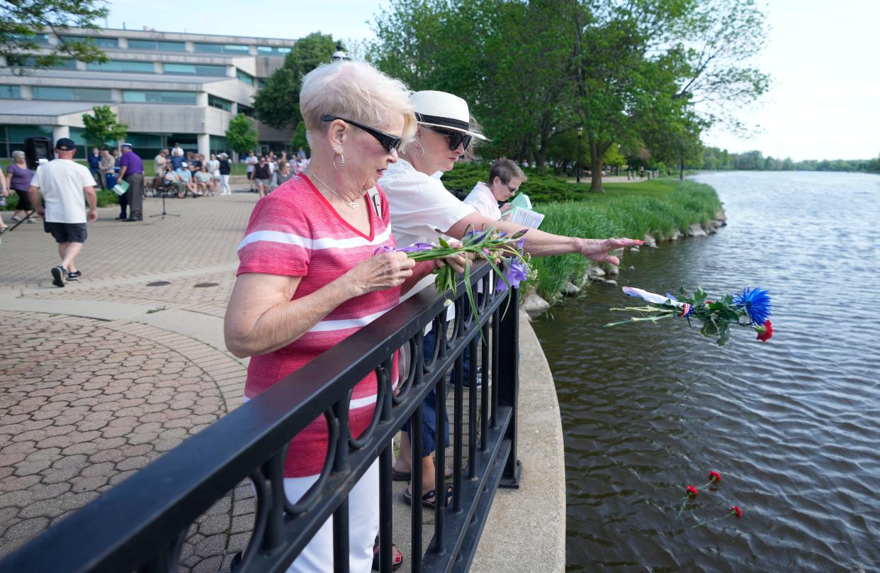 Kathy Fishel, second left, throws flowers into the Fox River to pay tribute to fallen service members along side Leigh Lanigan-Stanisch, left, during a River Service at the Lee Sherman Dreyfus State Office Building on Barstow Street prior to the Waukesha Memorial Day Parade in Waukesha on Monday, May 30, 2022. It’s the city’s first parade since the 2021 Christmas Parade tragedy.  Photo by Mike De Sisti / The Milwaukee Journal Sentinel