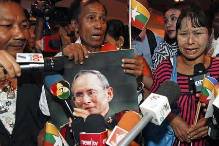 Tun Tun Htike (C), father of Win Zaw Htun, one of two Myanmar workers accused of killing British tourists holds a picture of Thailand's King Bhumibol Adulyadej as his wife May Thein (R) cries in front of reporters after arriving in Bangkok October 22, 2014. REUTERS/Chaiwat Subprasom