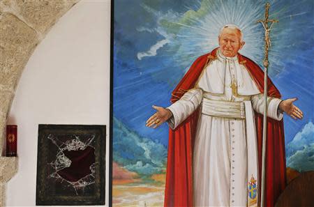 A broken glass of a niche where the reliquary with the blood of the late Pope John Paul II was located is seen next to a painting of the late Pope in the small mountain church of San Pietro della Ienca, near the city of L'Aquila January 28, 2014. Thieves broke into a small church in the mountains east of Rome over the weekend and stole the reliquary with the blood of the late Pope John Paul II, a custodian said on Monday. Dozens of police with sniffer dogs scoured the remote area for clues to what the Italian Catholic magazine Famiglia Cristiana called "a sacrilegious theft that was probably commissioned by someone". REUTERS/Max Rossi