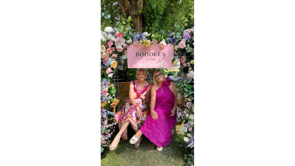 Penny Lancaster in a pink and red dress sitting under a floral arch