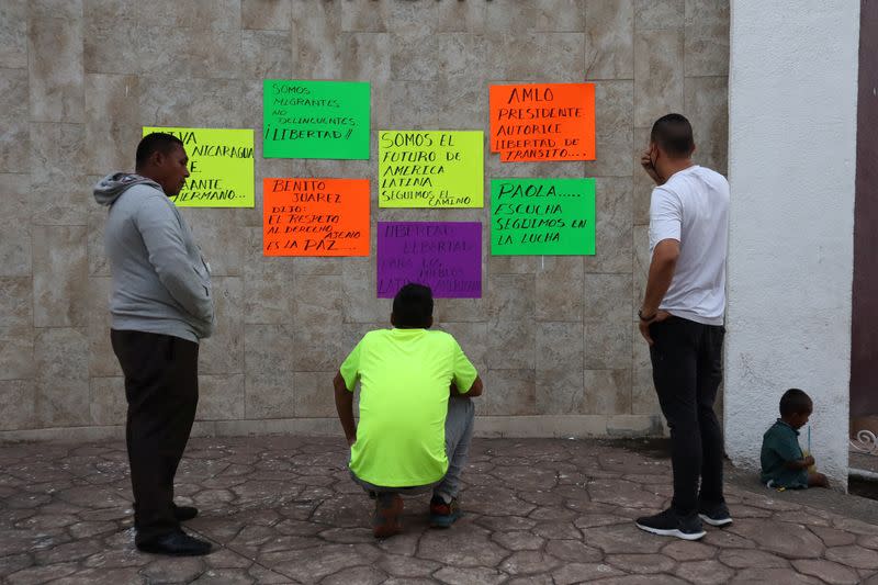 Migrants read signs as they gather at Benito Juarez square in Tapachula