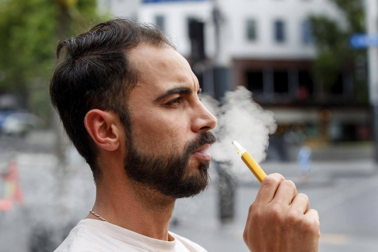 FILE - Vaping by a man in a street in Auckland, New Zealand, Thursday, Dec. 9, 2021. New Zealand on Tuesday passed into law a unique plan to phase out tobacco smoking by imposing a lifetime ban on young people buying cigarettes. (AP Photo/David Rowland, File)