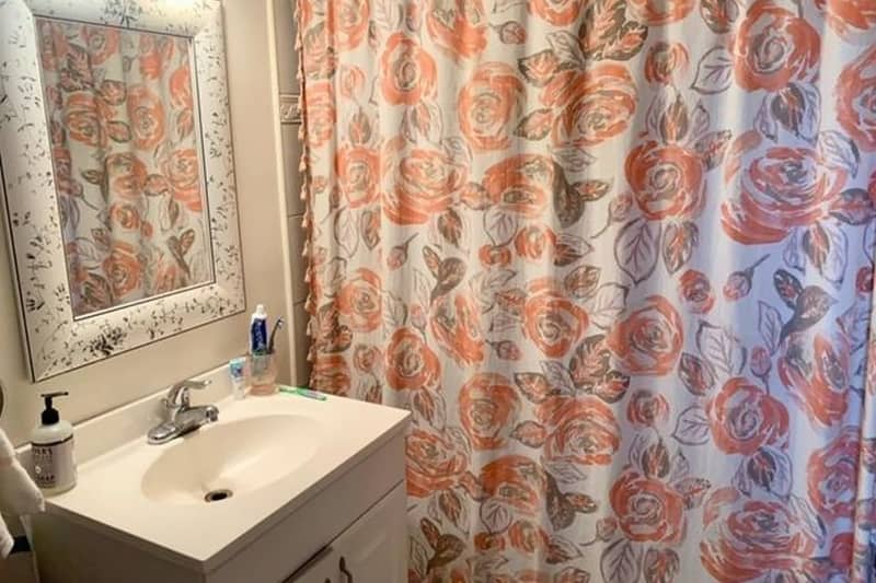 White bathroom with floral shower curtain and white and black framed mirror before makeover