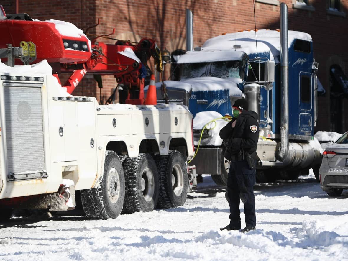 A police officer stands watch as a tow operator removes a truck from a blockade on Daly Avenue in Ottawa on Feb. 18. (Justin Tang/The Canadian Press - image credit)