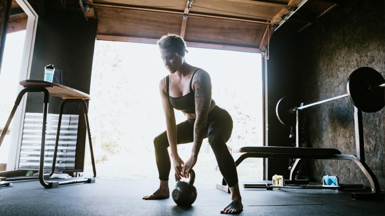  A woman working out in garage gym doing kettlebell squats. 