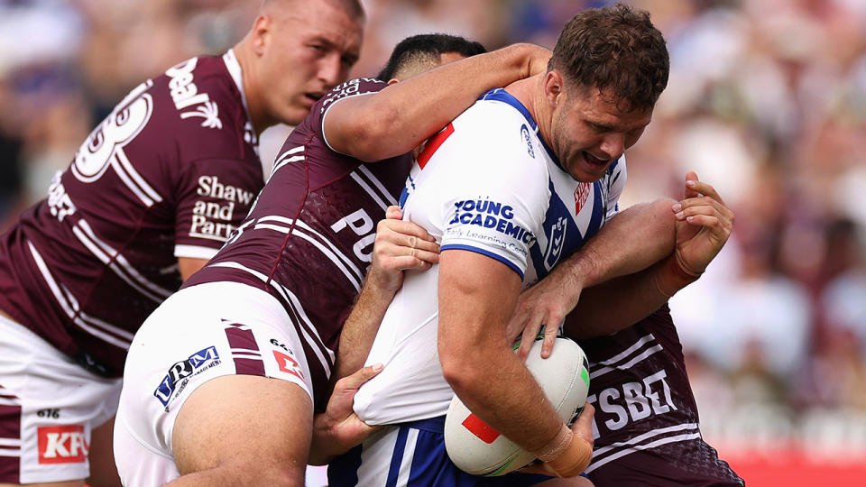 Corey Waddell tries to bust through a tackle laid by two Manly players.