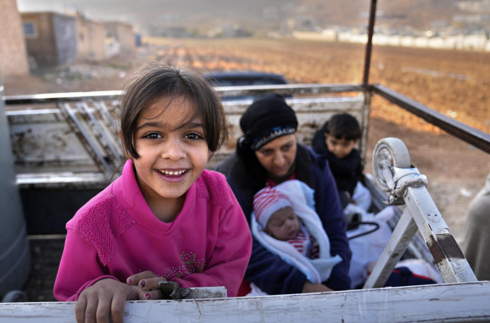 A Syrian refugee girl stands on a pickup next to her mother, as they wait at a gathering point to cross the border back home to Syria, in the eastern Lebanese border town of Arsal, Lebanon, Wednesday, Oct. 26, 2022. Several hundred Syrian refugees boarded a convoy of trucks laden with mattresses, water and fuel tanks, bicycles – and, in one case, a goat – Wednesday morning in the remote Lebanese mountain town of Arsal in preparation to return back across the nearby border.(AP Photo/Hussein Malla)