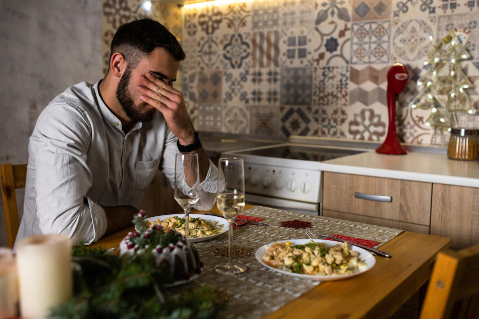 Man sitting at a table with a festive meal, appearing stressed or upset with his head in his hand