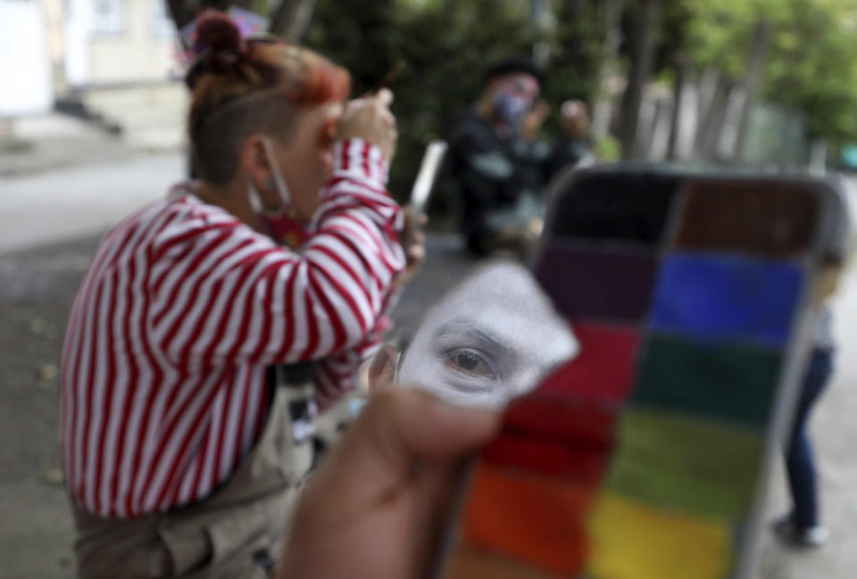 Integrante de la compañía de circo se refleja en un pedazo de espejo mientras se prepara para una presentación en la calle en la que su grupo conocido como "Circo Encuentro" actúa a cambio de donaciones de alimentos para ayudar a personas de bajo recursos en Bogotá, Colombia, el sábado 4 de julio de 2020. (Foto AP/Fernando Vergara)