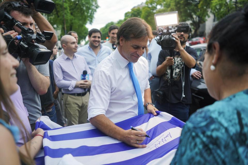 El candidato presidencial del Partido Nacional, Luis Lacalle Pou, firma una bandera nacional afuera de su sede de partido en Montevideo, Uruguay, el viernes 29 de noviembre de 2019. (AP Foto/Matilde Campodonico)