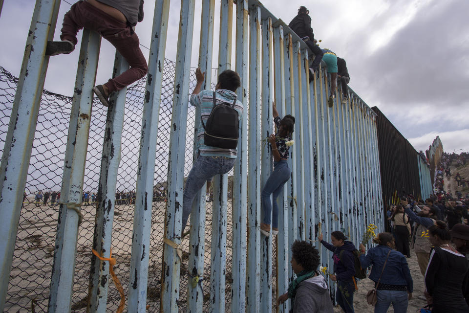 People climb a section of border fence to look into the U.S.