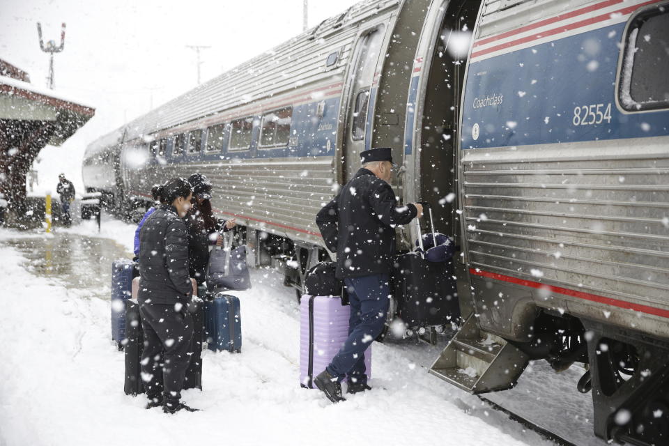 The conductor helps passengers board the southbound Amtrak Vermonter in Waterbury, Vt., during a snowstorm on Tuesday, March 14, 2023. The train was traveling during a winter storm that was dropping heavy, wet snow across the Northeast. The storm caused a plane to slide off a runway, led to hundreds of school closings, canceled flights and thousands of power outages in parts of the Northeast on Tuesday. (AP Photo/Wilson Ring)