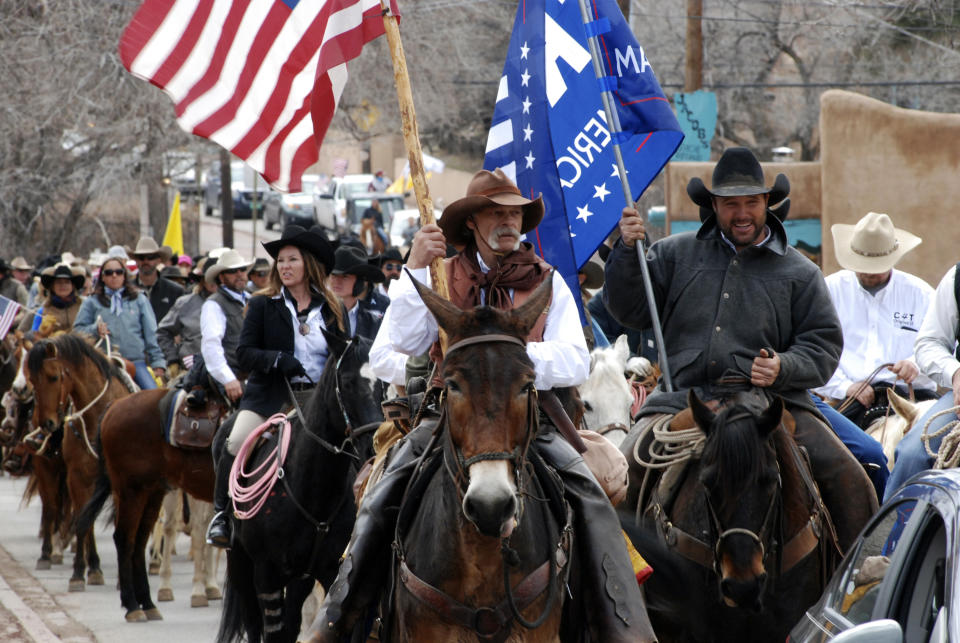 FILE - In this March 12, 2019 file photo, advocates for gun rights in New Mexico including rural ranchers joined with a interstate group called Cowboys for Trump, approach the New Mexico state Capitol in Santa Fe on horseback. Behind the raw public frustration and anger over election security that has played out this week in New Mexico was a hint of something deeper -- a growing divide between the state’s Democratic power structure and conservative rural residents who feel their way of life is under attack. (AP Photo/Morgan Lee, File)