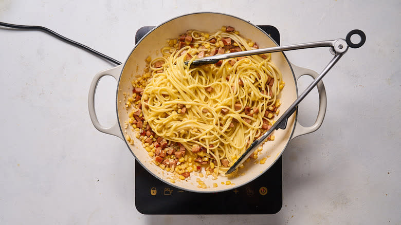 tossing pasta with sausage sauce in pan