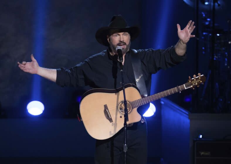 Garth Brooks holds his arms out onstage with a guitar slung around his body