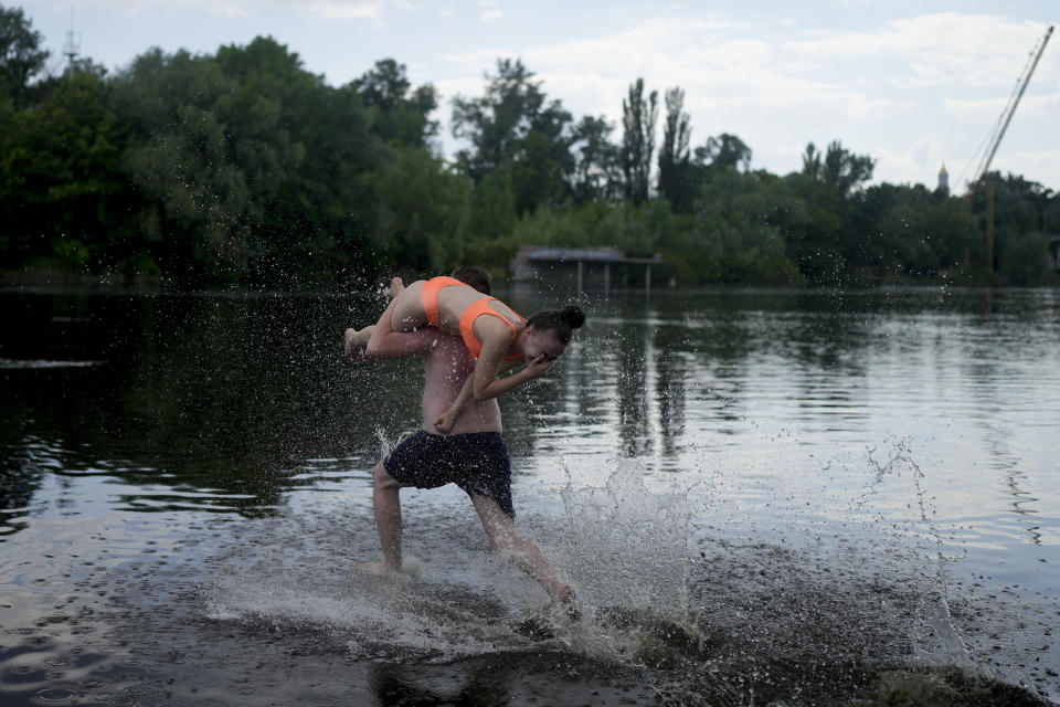 FILE - Valeria is carried by a friend as he runs in the Dnieper River in Kyiv, Ukraine, Thursday, June 9, 2022. With war raging on fronts to the east and south, the summer of 2022 is proving bitter for the Ukrainian capital, Kyiv. The sun shines but sadness and grim determination reign. (AP Photo/Natacha Pisarenko, File)