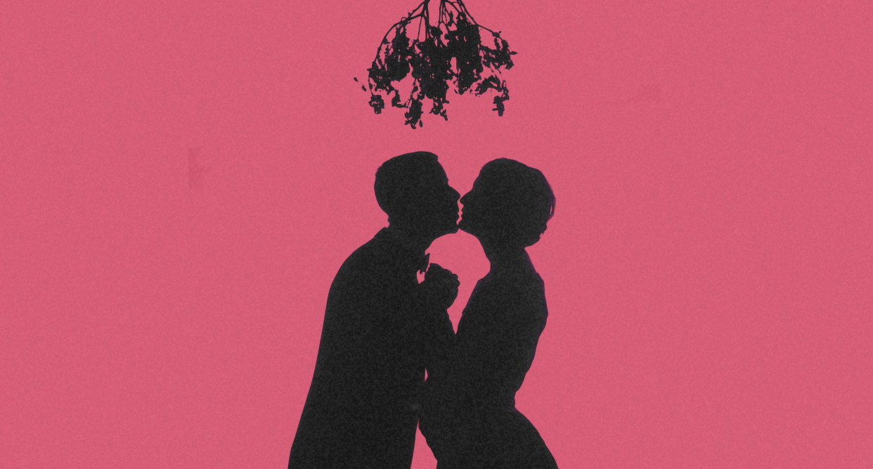 Silhouette of couple kissing under mistletoe with pink background.
