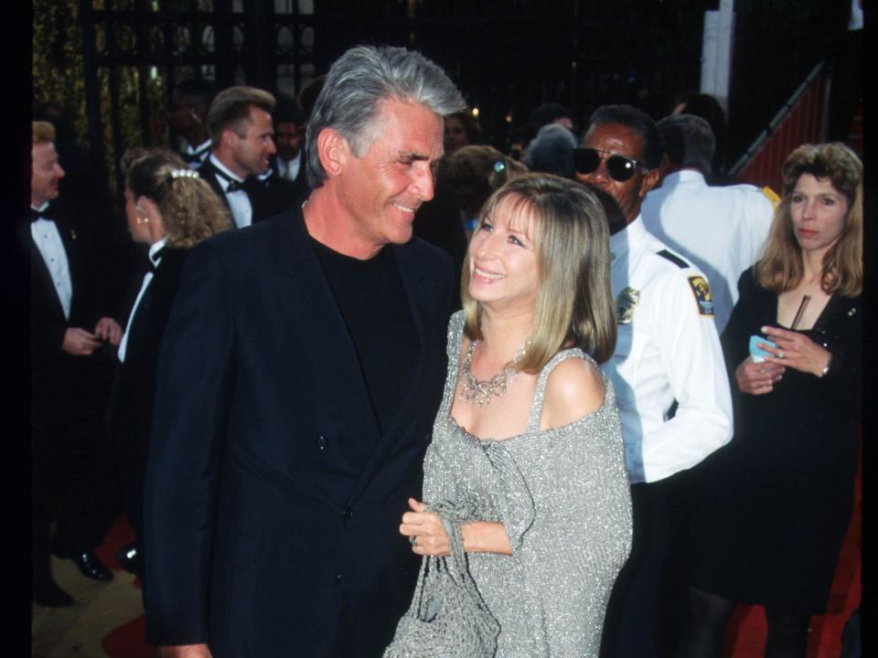 James Brolin, in a navy suit and black shirt, poses with Barbra Streisand, in a sparkly silver dress and shawl, on the red carpet at the 1997 Oscars.