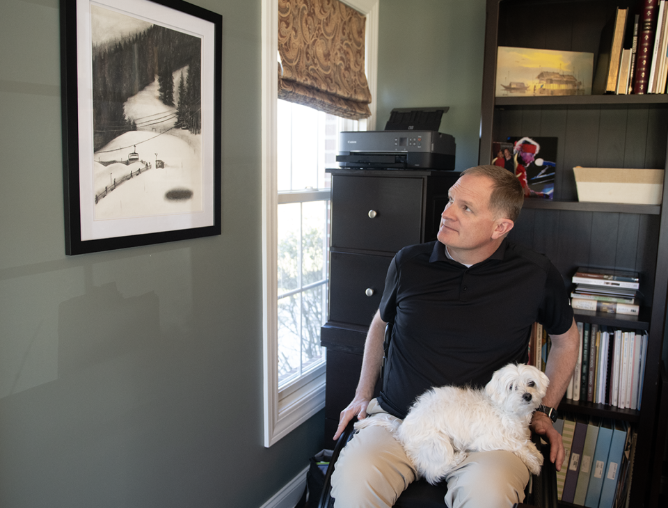 Jason Kolb looks at a charcoal drawing that hangs in his Kent home called "Sacred Ground" that shows where he had a skiing accident in Colorado that left him paralyzed. Daisy, the family's Coton de Tulear dog, sits on his lap. The drawing was done by artist Tara Deetscreek.