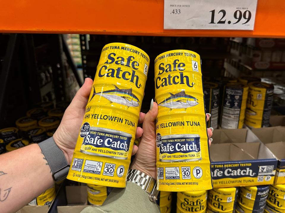 Two hands hold packages of tuna with yellow packaging and illustrations of tuna fish on them