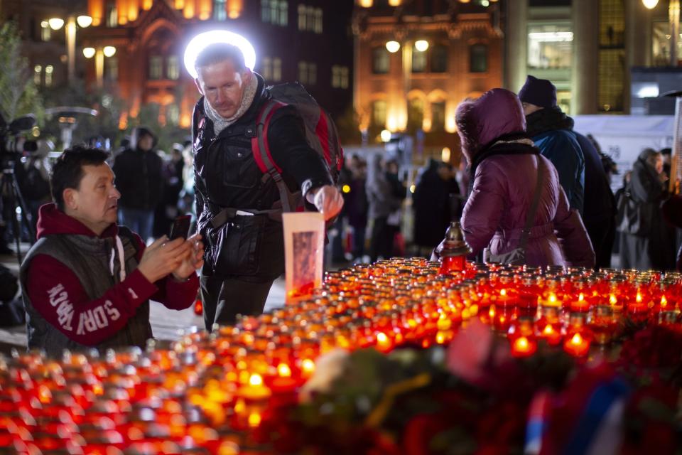 FILE - A man holds portrait of his relative, a victim of Soviet-era political repression, as other people lay flowers and light candles at a monument in front of the former KGB headquarters in Moscow, Russia, Monday, Oct. 29, 2018, in an annual commemoration of the victims of purges under Soviet dictator Joseph Stalin. Research and public debate about mass repressions by Soviet dictator Josef Stalin also have faced significant resistance in recent years. Historians and rights advocates say one reason is inevitable parallels to the ongoing government crackdown against dissent that has already landed hundreds of people behind bars. (AP Photo/Alexander Zemlianichenko, File)