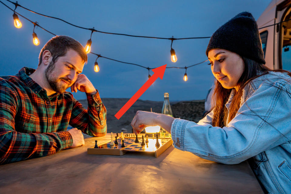 Edison bulbs hanging outside while a couple plays chess