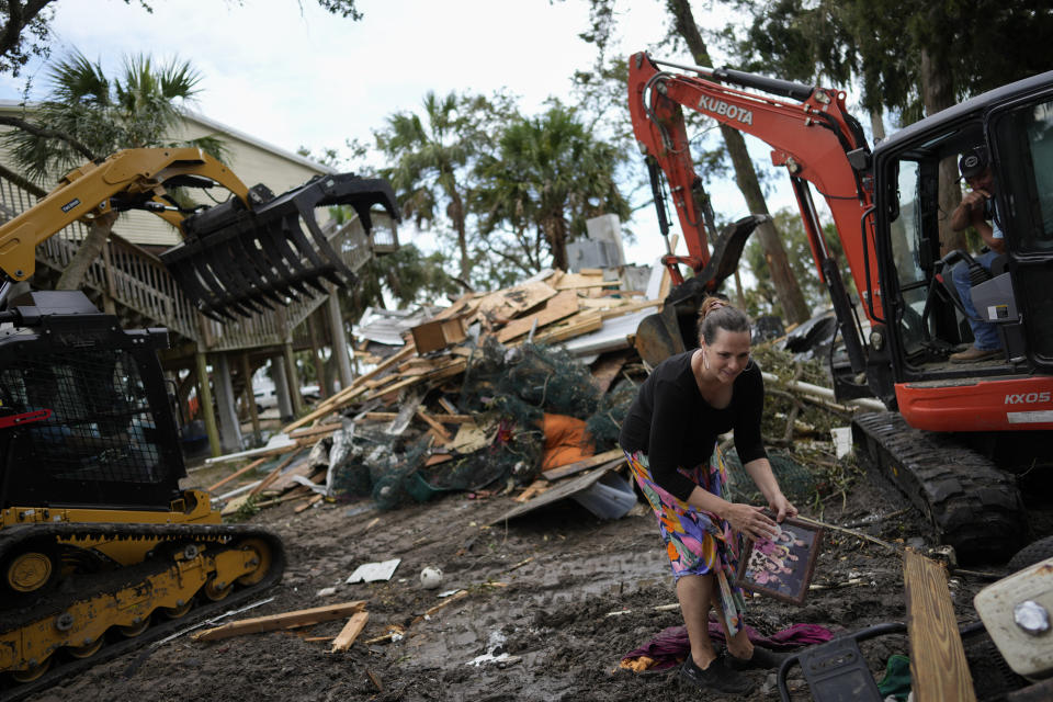 Stephanie Foley, 41, brushes mud off a framed picture of her and her sisters that was found among the wreckage of an old house which had served as a base for her father's crabbing business until being destroyed in Hurricane Idalia, in Horseshoe Beach, Fla., Friday, Sept. 1, 2023. Foley described Horseshoe Beach as a closely knit community where folks don't feel they have to lock their doors and you can go fishing anytime you want. But she fears that the traits that make the place special could vanish, with rebuilding prohibitively expensive for many of the longterm residents, and some new residents trying to change the character of the town away from one based on making a living on the water. (AP Photo/Rebecca Blackwell)