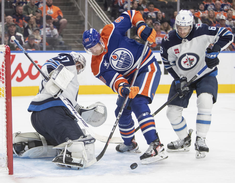 Winnipeg Jets goalie Connor Hellebuyck (37) stops Edmonton Oilers' Corey Perry (90) as Jets' Colin Miller (6) defends during second period NHL action in Edmonton, Alberta, Wednesday, Oct. 9, 2024. (Amber Bracken/The Canadian Press via AP)