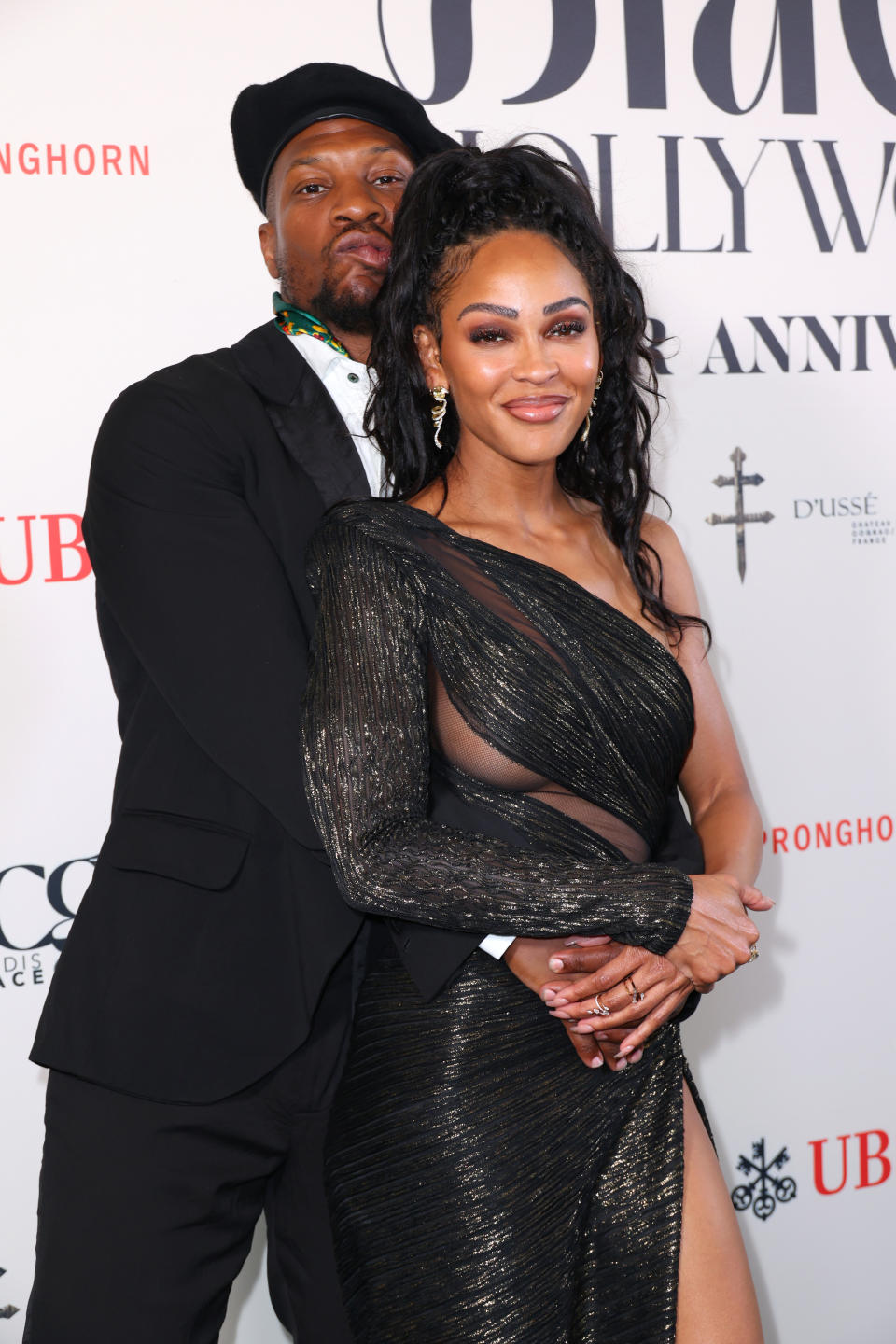 Meagan Good and Jerrie Johnson pose on the red carpet. Meagan is in a glamorous, one-sleeve, black-sequined gown with sheer panels