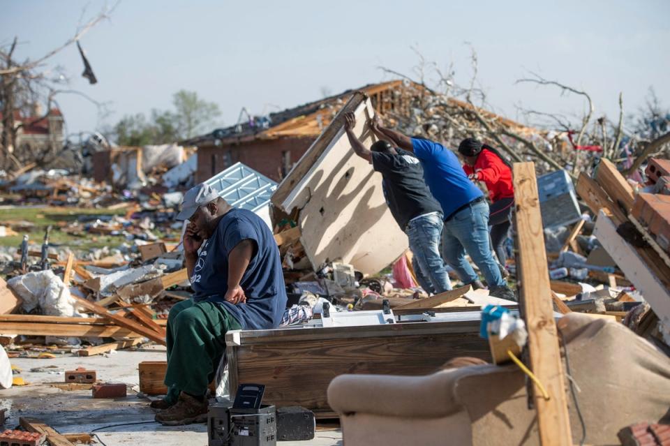 Wendell Sturdevant, of Rolling Fork, Miss., calls his wife as friends and his niece search through the rubble of what was a Blue Front Apartments duplex unit that he and his mother lived in