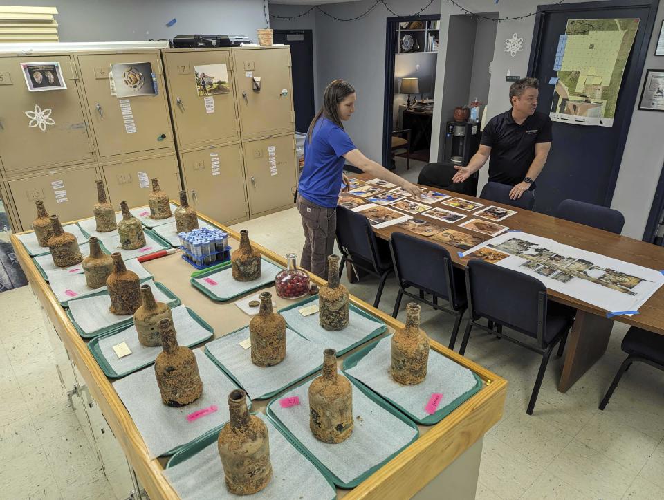 Archeologist Jason Boroughs, right, and curator Lily Carhart, left, point to photographs of a few dozen 18th-century glass bottles containing fruit that were unearthed in the cellar of George Washington's residence in Mount Vernon, Va., Monday, June 17, 2024. (AP Photo/Nathan Ellgren)