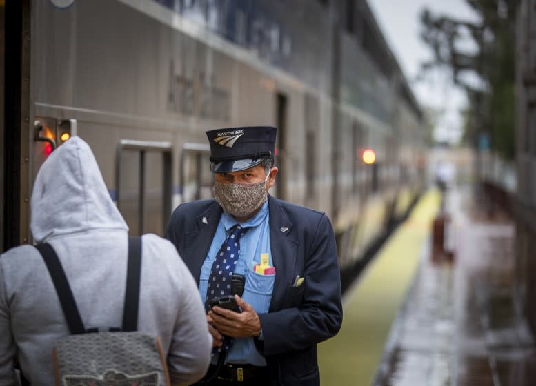 SANTA ANA, CA -- THURSDAY, APRIL 9, 2020: An Amtrak officer wears a protective mask while checking passengers boarding the train at the Santa Ana Regional Transportation Center amid coronavirus (COVID-19) physical distancing restrictions in Santa Ana, CA, on April 9, 2020. (Allen J. Schaben / Los Angeles Times)