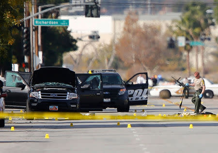 A police officer picks up a weapon from the scene of the investigation around the area of the SUV vehicle where two suspects were shot by police following a mass shooting in San Bernardino, California December 3, 2015. REUTERS/Mike Blake