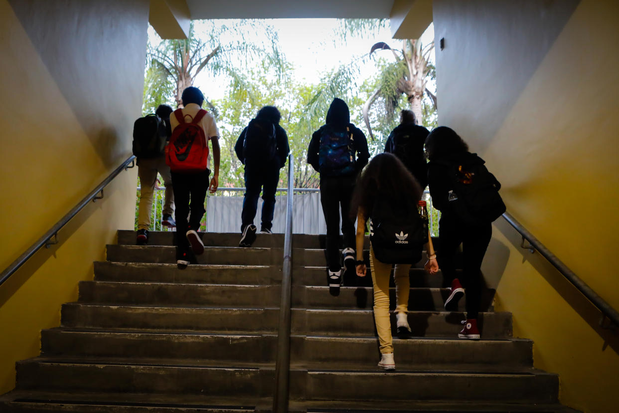 Students wearing backpacks walk up a set of stairs at a school.