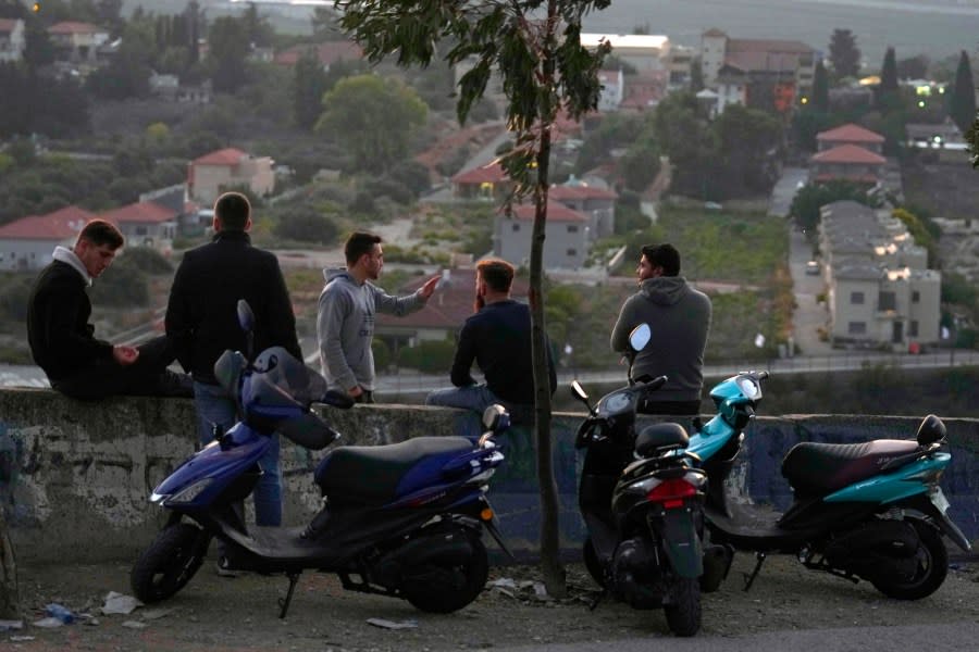 Lebanese men sit facing the Israeli town of Metula, background, in the southern border village of Kfar Kila, Lebanon, Thursday, Oct. 12, 2023. (AP Photo/Bilal Hussein)