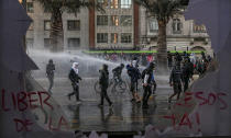 Anti-government protesters are sprayed by police with water during a protest against police in reaction to a video that appears to show an officer pushing a youth off a bridge the previous day at a protest, in Santiago, Chile, Saturday, Oct. 3, 2020. (AP Photo/Esteban Felix)