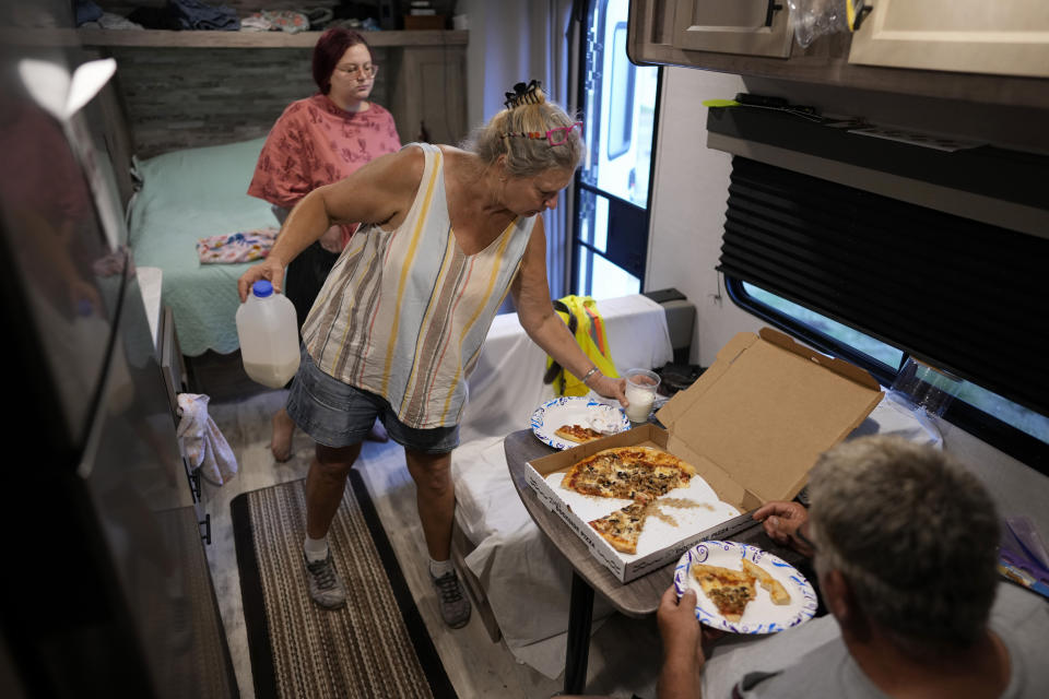Jacquelyn, center, and Timothy Velazquez share a pizza inside the small camper where they are living with their daughter Hannah, top, home from college and working for the summer, while they wait to be able repair their home, which was damaged when Hurricane Ian's storm surge rose to within inches of their ceiling, in Fort Myers Beach, Fla., Wednesday, May 24, 2023. (AP Photo/Rebecca Blackwell)