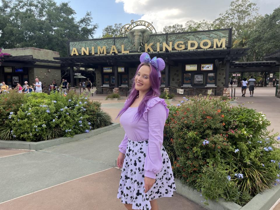 Author wearing purple shirt, purple Mickey ears, and cow-print skirt standing in front of Animal Kingdom sign.