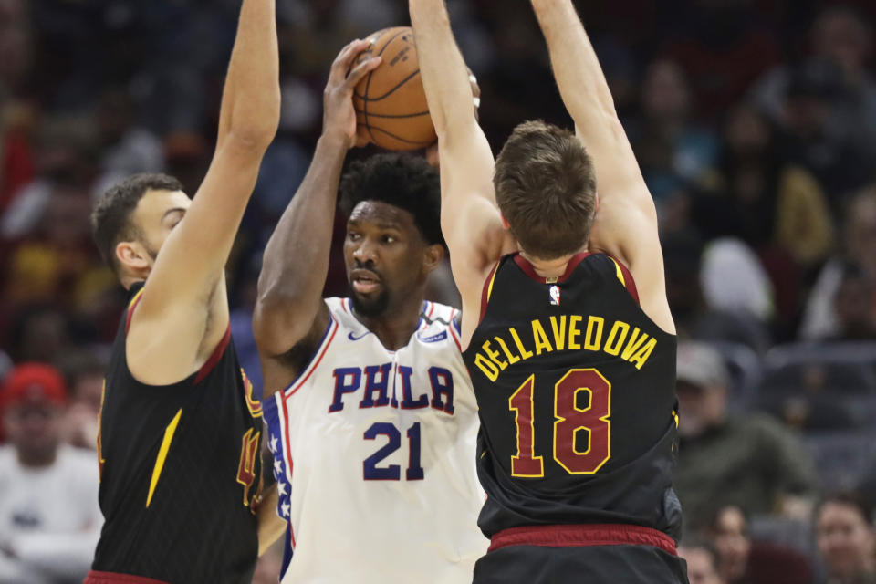 Philadelphia 76ers' Joel Embiid, center, squeezes between Cleveland Cavaliers' Ante Zizic, left and Matthew Dellavedova in the first half of an NBA basketball game, Wednesday, Feb. 26, 2020, in Cleveland. (AP Photo/Tony Dejak)