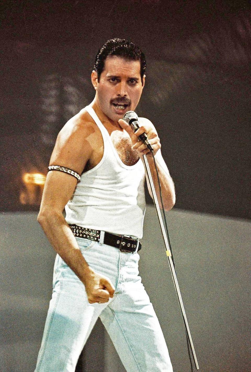 freddie mercury sings into a microphone he holds on a stand