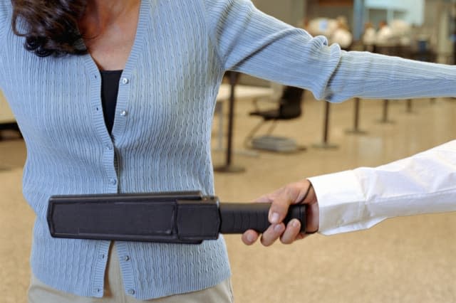 Woman being swiped by metal detector at airport security checkpoint