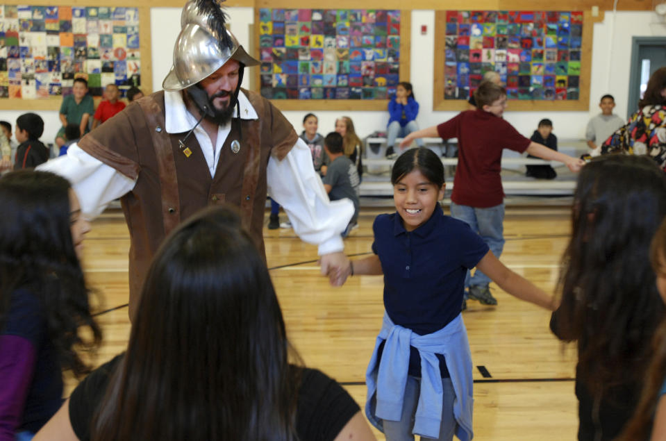 FILE - In this Wednesday, Aug. 30, 2017 file photo, Edwin Quintana, left, dressed as a 17th Century Spanish conquistador, dances with fifth grader Kaylee Pacheco and other students at Tesuque Elementary school in Tesuque, N.M. In recent years, the conquistador and all the effigies connected to it have come under intense criticism from Native American activists who say the image glorifies indigenous genocide and needs to be removed from schools, streets and seals. (AP Photo/Morgan Lee,File)