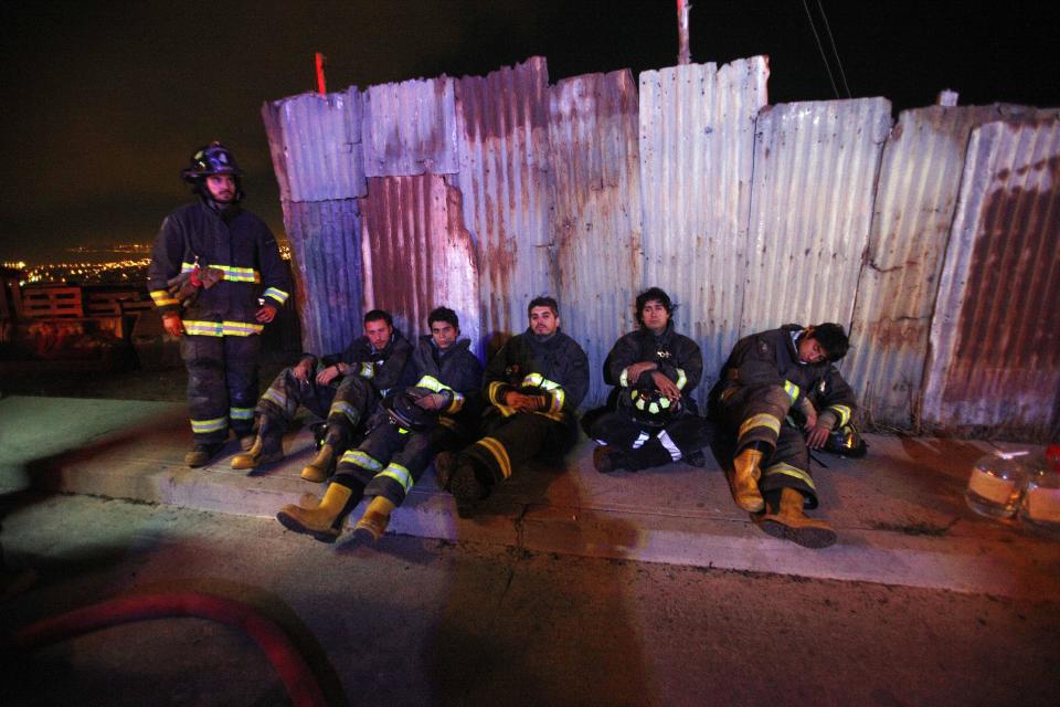 Firefighters take a break from battling blazes after an out of control forest fire reached urban areas in the city of Valparaiso, Chile, early Monday April 14, 2014. Firefighters struggled for a second night to contain blazes that reached this port city, killing at least a dozen people, destroyed hundreds homes and has forced the evacuation of thousands. (AP Photo/Luis Hidalgo)