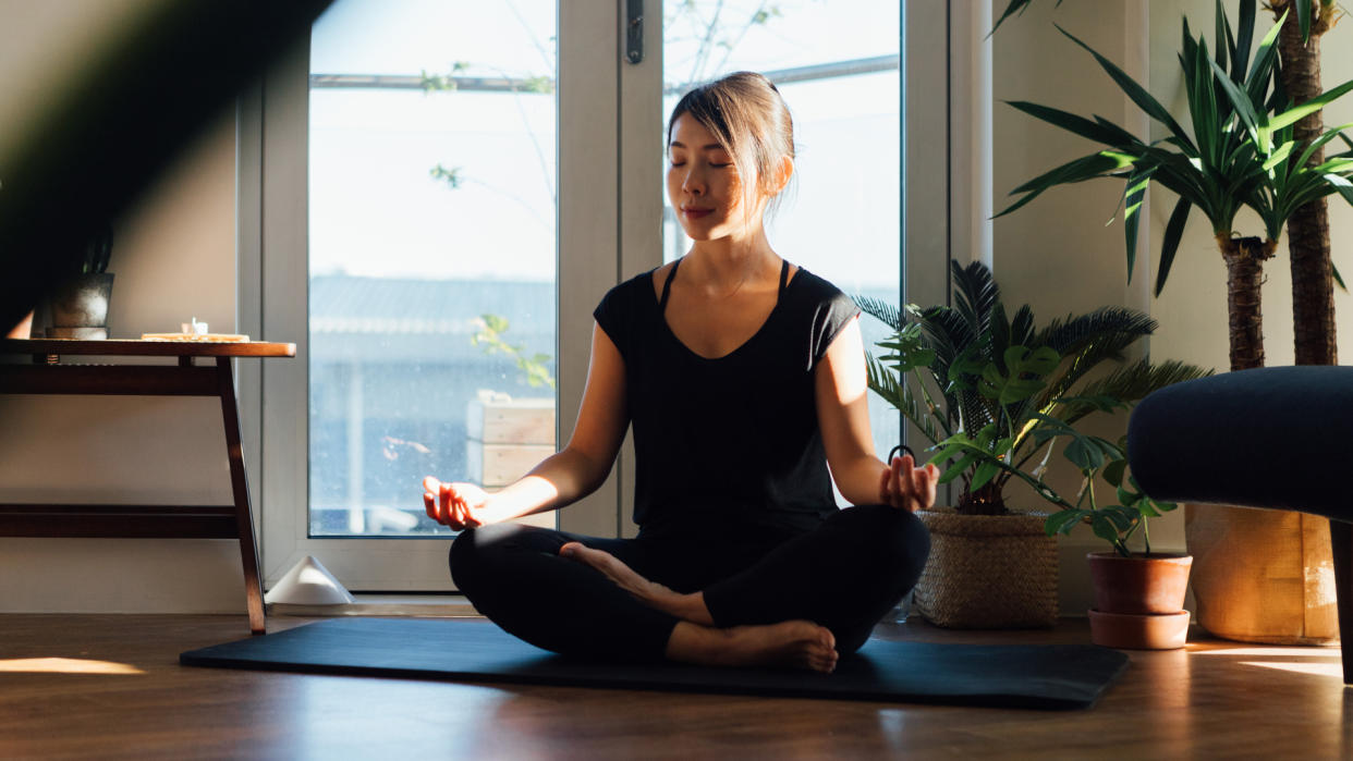  A woman meditating on her yoga mat at home. 