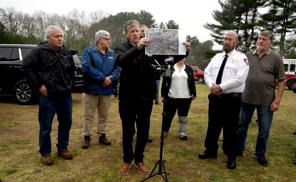 Gov. Dan McKee, standing with state environmental and emergency-management officials and Exeter Fire and Rescue Chief Scott Gavitt, right, holds up a photo of damage from last Friday's brush fire after he toured the area on Monday.,