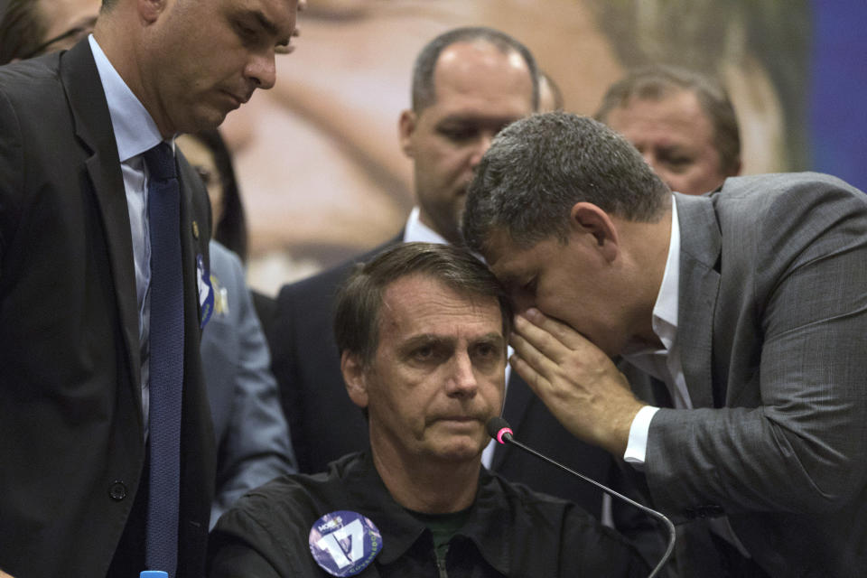 Gustavo Bebianno Rocha, right, president of the right wing Social Liberal Party, whispers to his presidential candidate Jair Bolsonaro, of the Social Liberal Party as his son Flavio Bolsonaro, left, stands aside during a press conference in Rio de Janeiro, Brazil, Thursday, Oct. 11, 2018. Bolsonaro will face Workers Party presidential candidate Fernando Haddad in a presidential runoff on Oct. 28. (AP Photo/Leo Correa)
