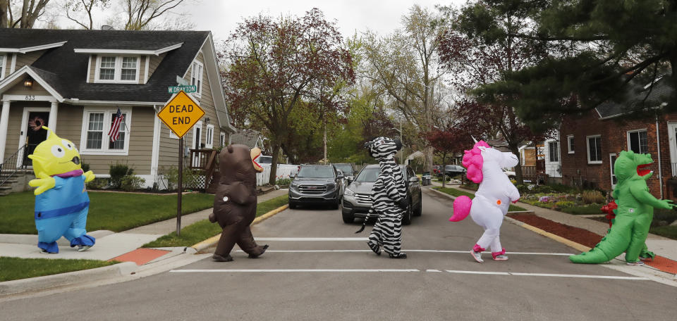 In this Monday, May 11, 2020 photo, members of the T-Rex Walking Club walk through a neighborhood in Ferndale, Mich. While the club members get a kick out of their strolls through town, the idea is to bring a little bit of cheer to their fellow residents who remain under quarantine as part of Gov. Gretchen Whitmer’s stay-at-home order due to the COVID-19 pandemic. (AP Photo/Carlos Osorio)